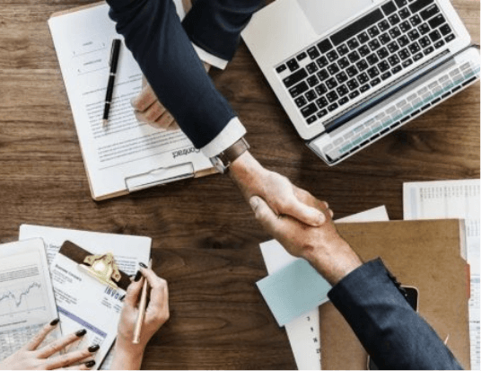 Top view of two men shaking hands in agreement over a desk.